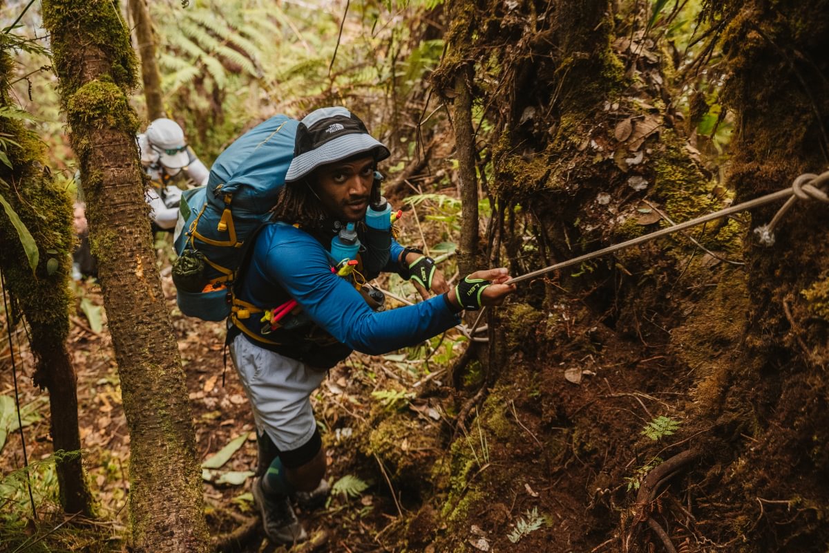 A runner using a rope to climb through dense jungle during the BTU Jungle Ultra, Peru